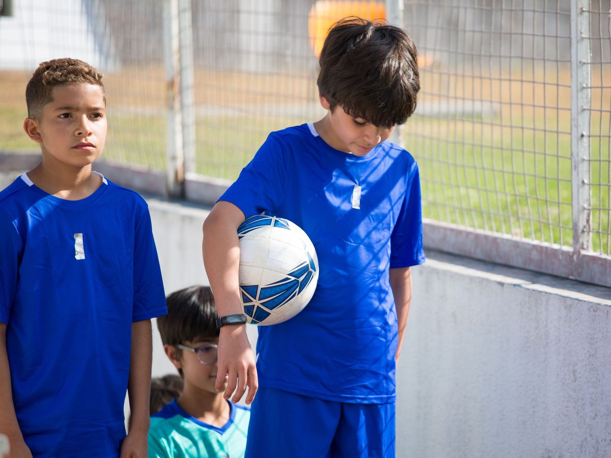 Young football players waiting by the pitch, one looking towards the stands