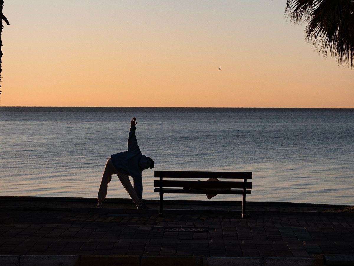 A person stretching by the sea at sunrise between two palm trees
