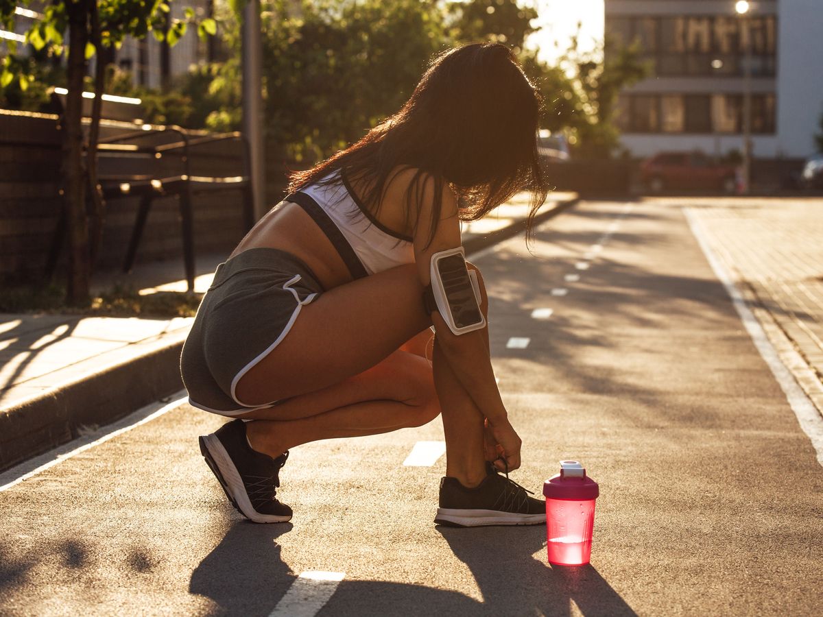 A woman tying her running shoes on an empty street at sunrise